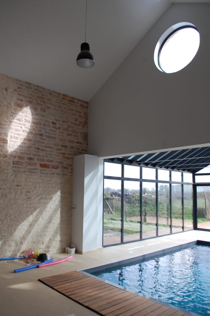 Rénovation et extension d'une longère. Vue intérieure de l'extension avec piscine intérieure couverte par une véranda.